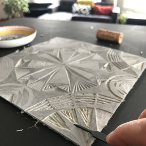 Close-up of the process of carving linoleum. A geometric design is partially carved into a piece of linoleum.