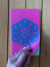 Load image into Gallery viewer, A medium pink Moleskine journal hand printed with a geometric pattern with blue ink. Open to show it is ruled.