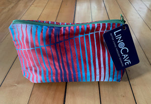 A red silk toiletry bag with a dark green zipper hand block printed with an ombre of colors ranging from light to dark blue.