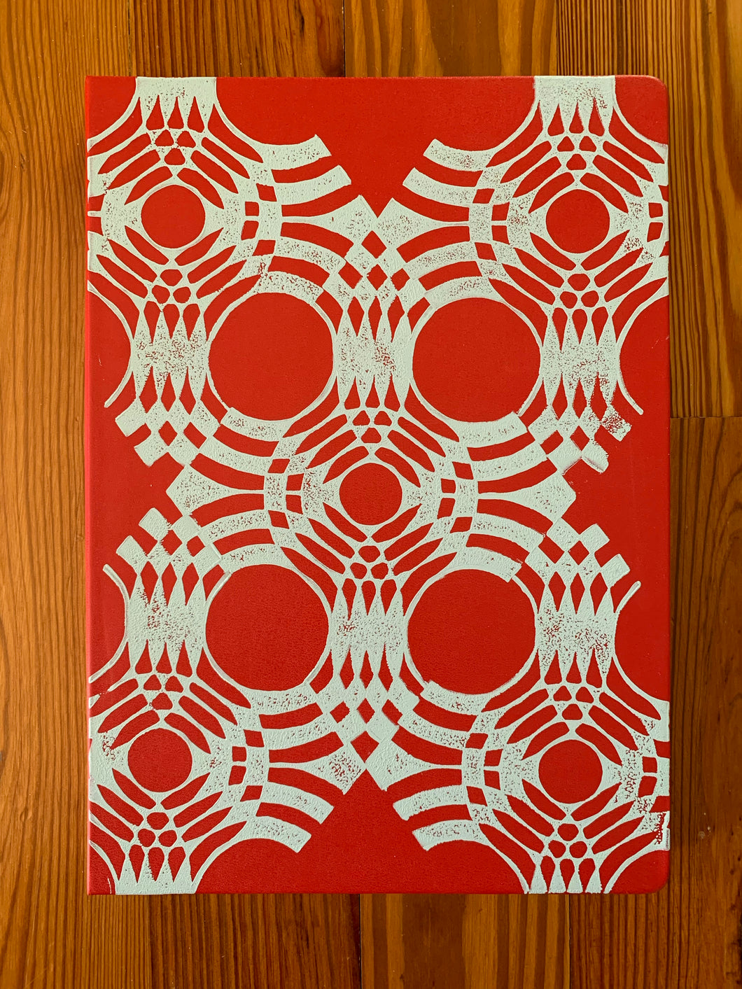 A red Moleskine sketchbook hand block printed in a white geometric pattern.